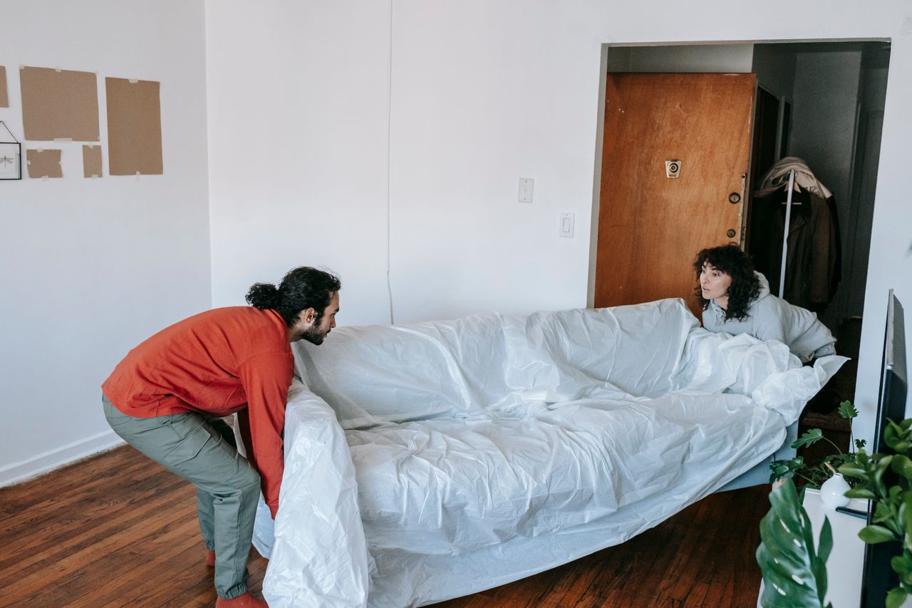 Two people working together to carry a sofa as they settle into a new apartment.
