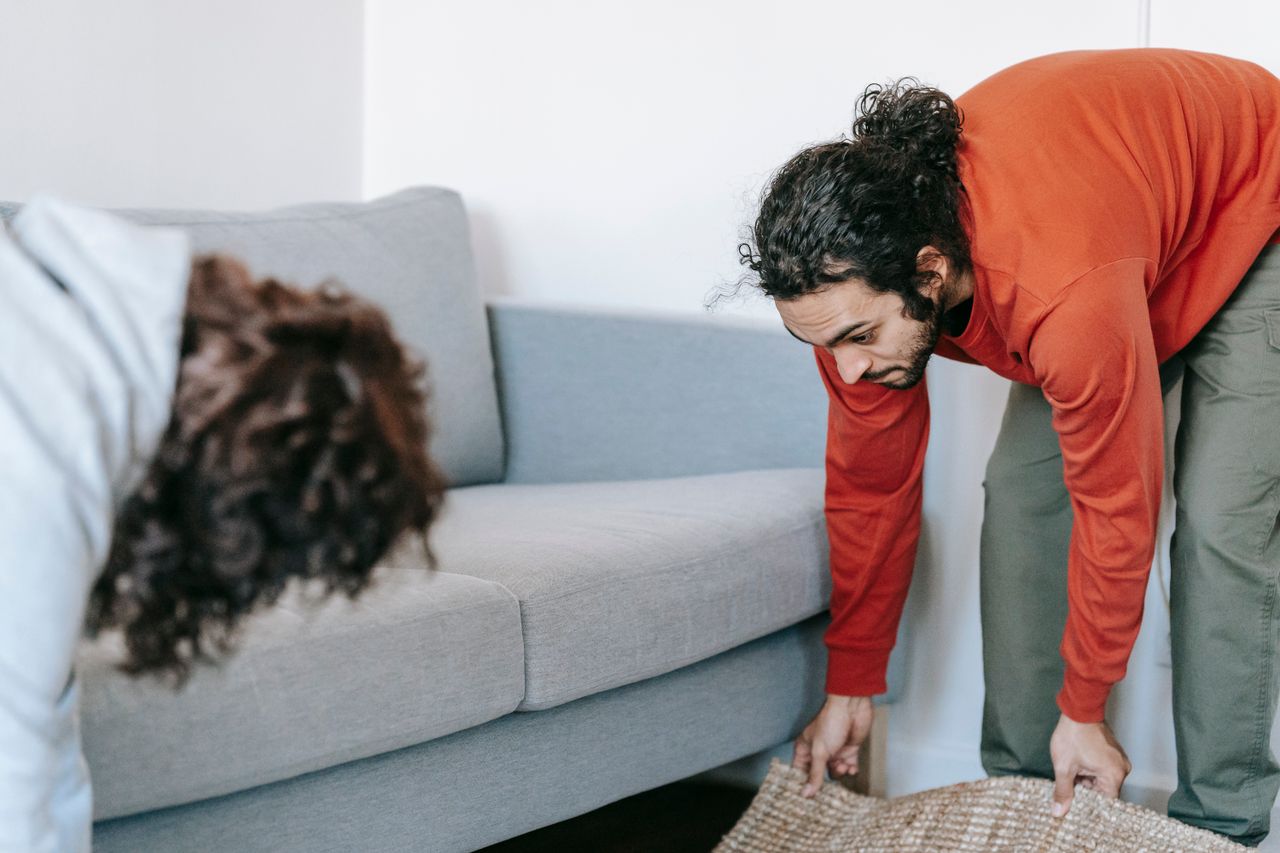 Un couple rangeant son salon, en remettant en ordre les meubles et les tapis avec esprit d’équipe.